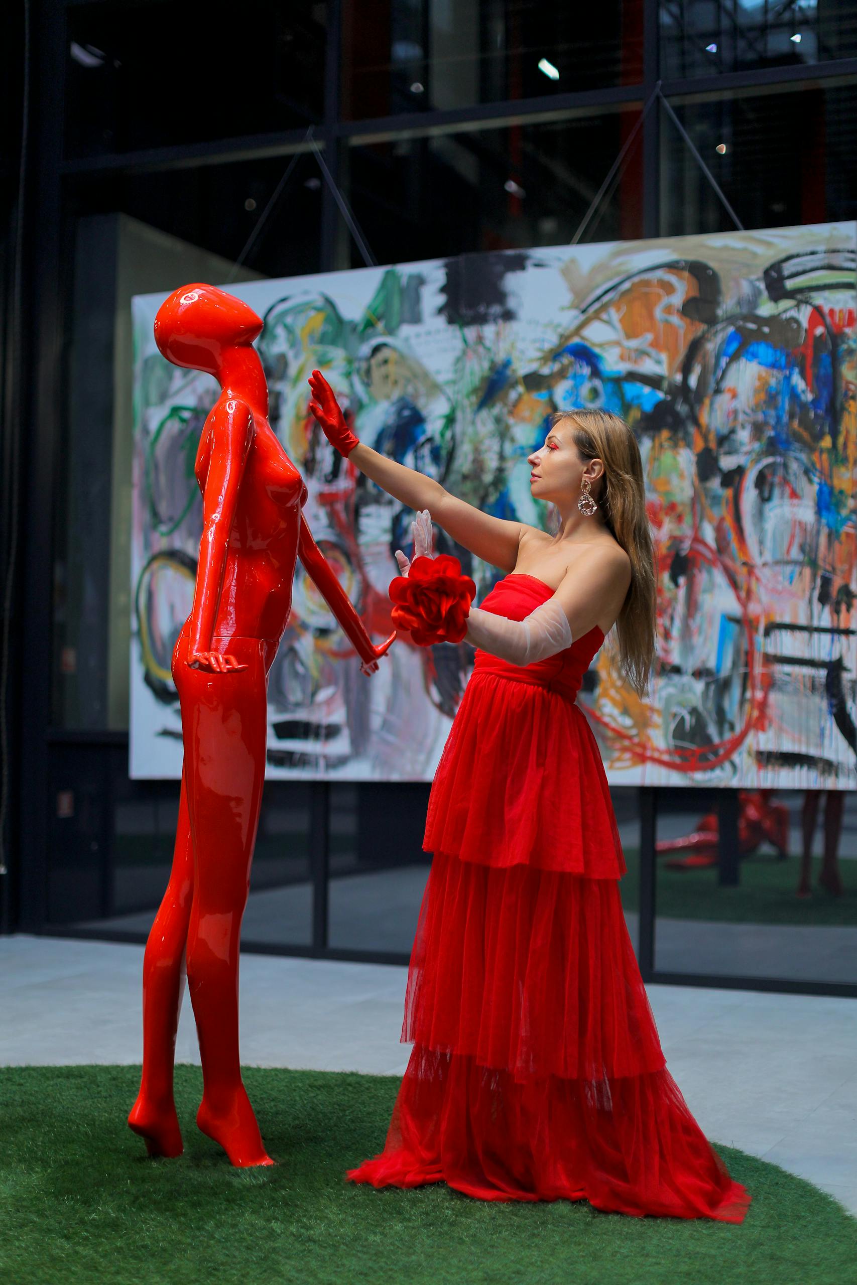 Woman in red dress interacting with a red modern art sculpture indoors.